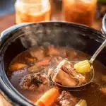 Warm homemade beef bone broth in a jar with rich golden color and fresh herbs.