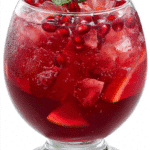 A bright red holiday punch served in a goblet-style glass with ice and a mint garnish on a clean white background.